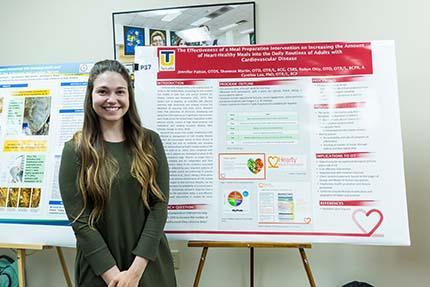 A student stands next a poster board on a stand featuring a research project.