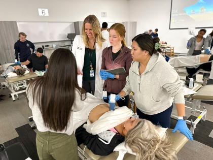 A faculty member and three students use a handheld ultrasound on a student lying on a medical table.