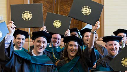 Students raise their diplomas during commencement.