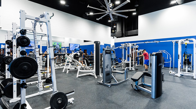 An indoor fitness room wish various weight machines and free weights. A few students are scattered around the room, using the equipment.